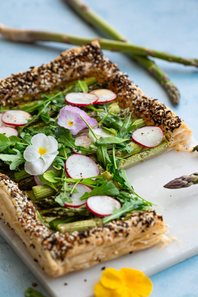 Sluoksniuotos tešlos tarta su smidrais, ridikėliais, šviežiais žalumynais, pertepta pesto kremu, papuošta gėlėmis.
